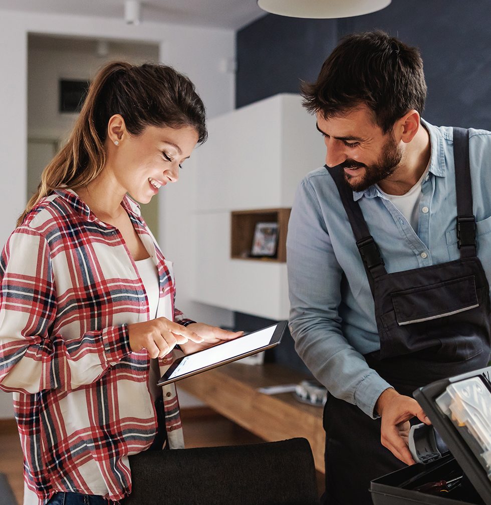 Smiling housewife paying repairman over tablet while repairman collecting his tools.